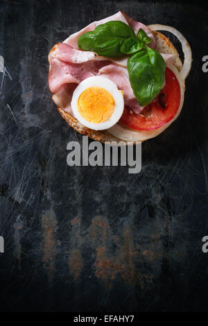 Sandwich with ham, eggs, vegetables and ketchup over black metal background. Top view Stock Photo