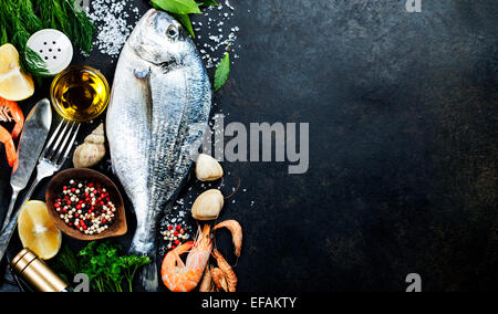 Delicious fresh fish on dark vintage background. Fish with aromatic herbs, spices and vegetables - healthy food, diet or cooking Stock Photo