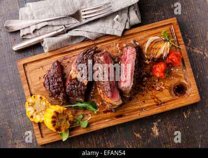 Sliced medium rare grilled Beef steak Ribeye with corn and cherry tomatoes on cutting board on wooden background Stock Photo