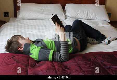Young teenage boy reading book whilst laying on a bed Stock Photo