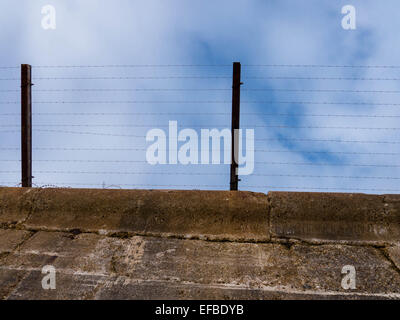 A barbed wire fence on top of a concrete wall Stock Photo