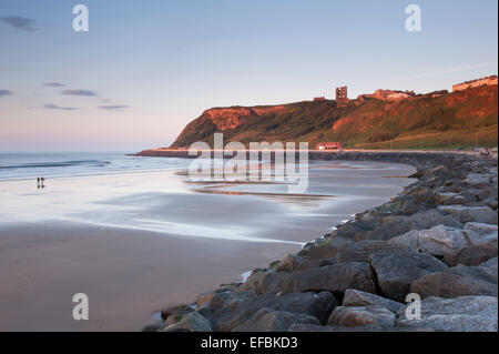 Picturesque view of blue evening sky, smooth, flat, sandy beach, calm sea & sunlit castle on cliff - North Bay, Scarborough, Yorkshire, England, UK.