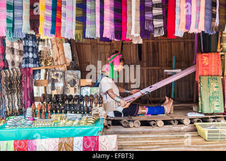 Long neck Burmese woman in a colourful headdress at Karen Padong village near Chiang Rai, Thailand, weaving at a hand loom