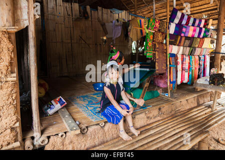 Cute young Burmese long neck girl sitting outside her mother's fabric shop hut in Karen Padong village, Chiang Rai, Thailand Stock Photo