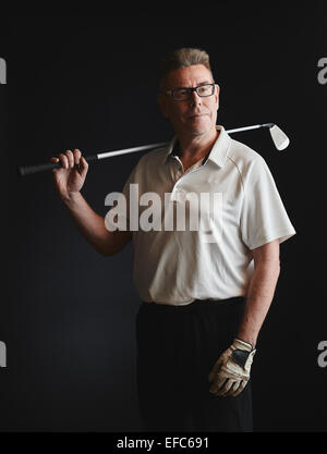 Mature man golfer wearing a white shirt and hold a iron golf club on his shoulder - studio shot, black background Stock Photo