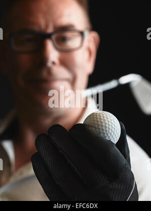 Close up, mature man golfer wearing a white shirt and he holds a golf ball on hand, iron golf club on his shoulder - focus on ba Stock Photo