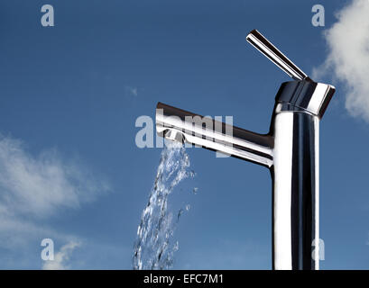 A faucet with water running, shown against a blue lightly clouded sky indicating freshness, purity, wastage etc. Stock Photo