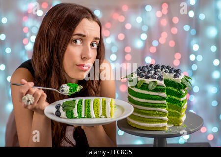 Sad girl thinking eat or not to eat happy birthday cake sitting on festive light background Stock Photo