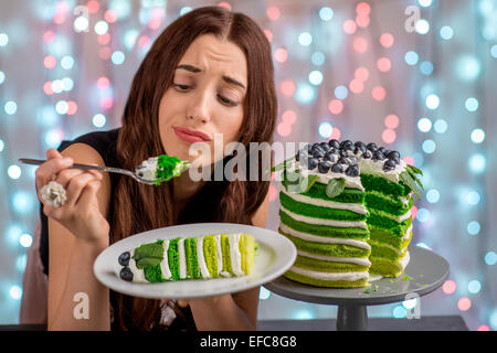 Sad girl thinking eat or not to eat happy birthday cake sitting on festive light background Stock Photo