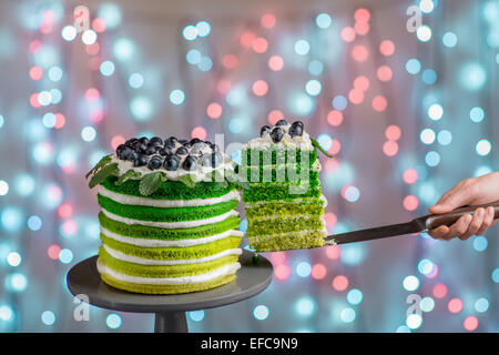 Cutting beautiful green sponge cake on festive background with bokeh light Stock Photo