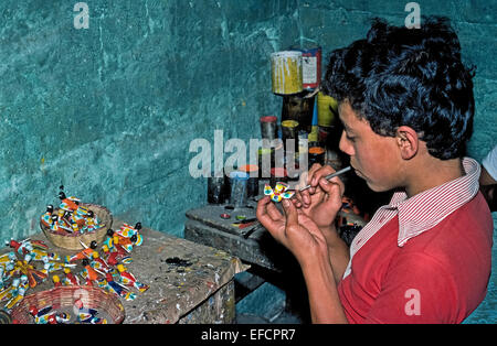 A young boy carefully applies colorful paints to tiny bird figurines made of clay in a pottery factory in Antigua, Guatemala. Stock Photo