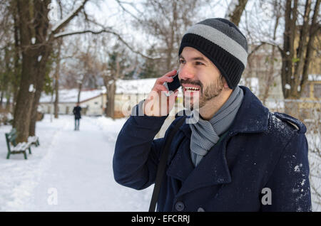 Young bearded male talking on his smart phone, outdoors in the snow Stock Photo