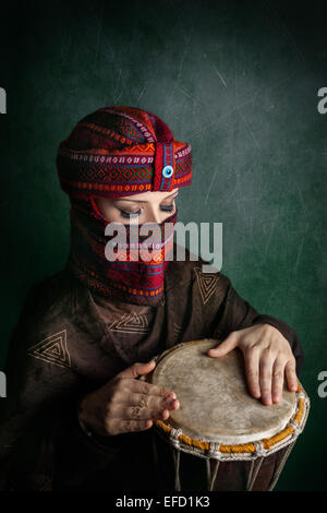 Oriental woman in turban playing drum at green textured wall Stock Photo