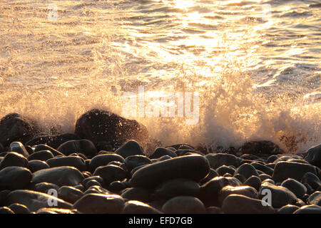 Wave breaking over pebble beach at dusk Stock Photo