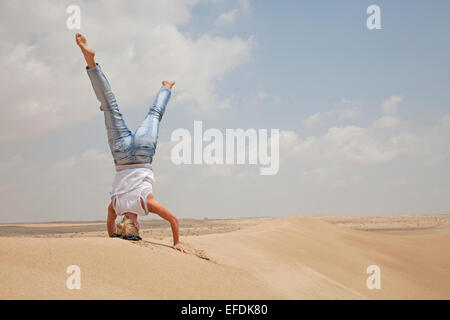 Woman doing headstand/yoga on sand dune in desert, Dubai, United Arab Emirates Stock Photo
