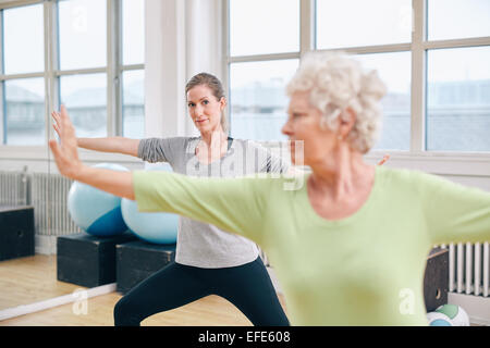 Two women doing stretching and aerobics workout at gym. Female trainer in background with senior woman in front during physical Stock Photo