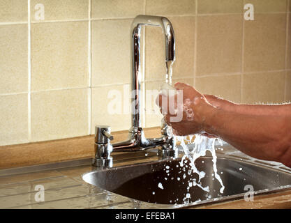 A man washes his hands under a running  faucet; this image is back lit to show detail in the water Stock Photo