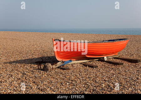 Small orange fishing or rowing boat on shingle beach, Brighton, England Stock Photo