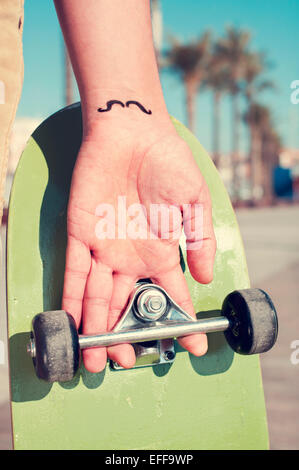 closeup of a young man with a moustache tattooed in his wrist holding a skateboard Stock Photo