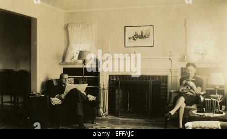 Dec. 12, 2014 - CANADA - CIRCA 1960s: Reproduction of an antique photo shows Man and woman sitting in a chair near the fireplace. A man reads a newspaper, woman knits on the needles. (Credit Image: © Igor Golovniov/ZUMA Wire/ZUMAPRESS.com) Stock Photo