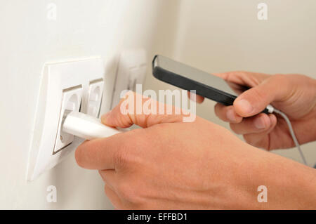 closeup of the hands of a man plugging in the plug of his smpartphone in a socket Stock Photo
