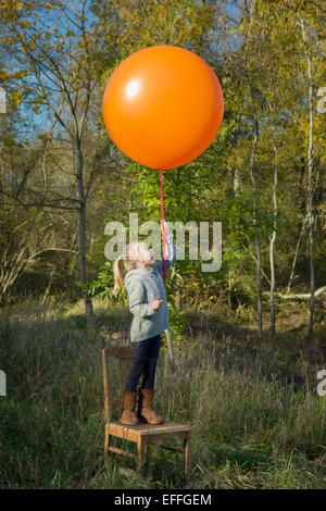 Girl standing on chair holding balloon on meadow Stock Photo