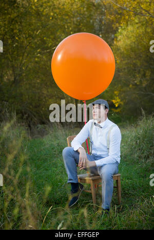 Man sitting on chair with balloon on meadow Stock Photo