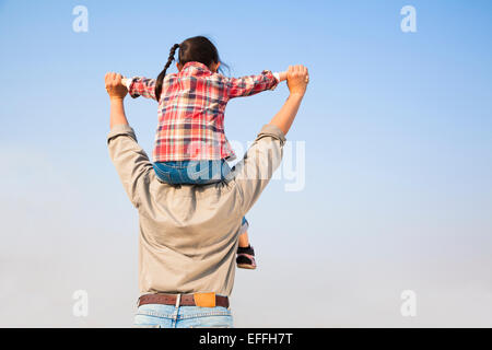 Father carrying his daughter on shoulders with blue sky background Stock Photo