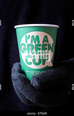 I'm a green cup printed on the front of a 100% compostable cardboard cup kind to the environment. Held in man's gloved hand Stock Photo