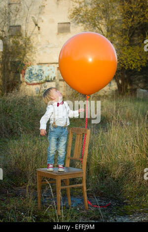 Boy standing on chair with balloon on meadow Stock Photo