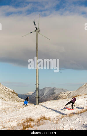 Wind turbines on Kirkstone Pass, which power the Kirkstone Pass Inn, in the Lake District, UK, with folk sledging in the snow Stock Photo