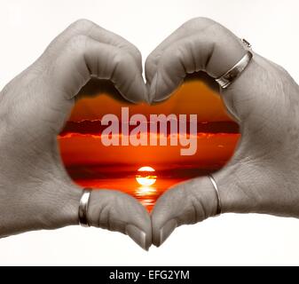 Female hands in a heart shape with a sunset digitally added Stock Photo