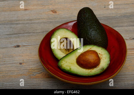 whole avocado and two halves on a red ceramic bowl Stock Photo