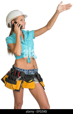 Woman in hard hat calling on mobile phone and showing direction Stock Photo
