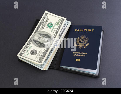 A United States of America Passport in a leather holder with several hundred dollar bills atop a dark background. Stock Photo