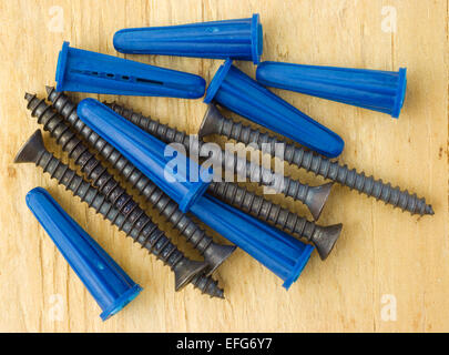 A group of blue plastic wall anchors with screws on a plywood work bench. Stock Photo