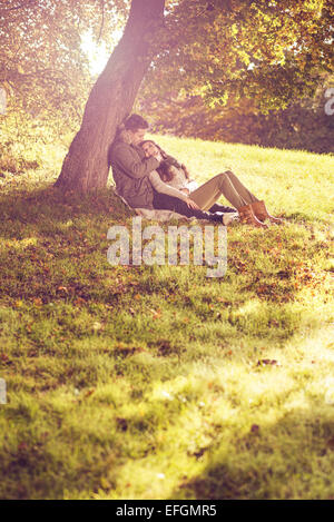 Love couple sitting under a tree in the colorful  autumn forest Stock Photo