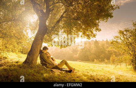 Loving couple under a big tree in the park in autumn Stock Photo