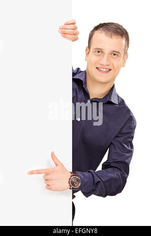 Young guy posing behind a panel and pointing with his finger isolated on white background Stock Photo