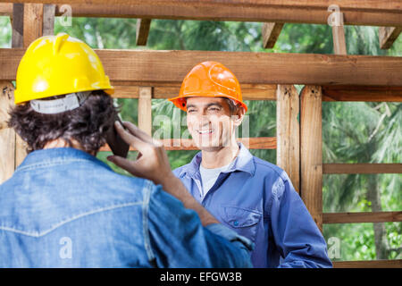 Happy Architect Looking At Colleague Using Cellphone Stock Photo