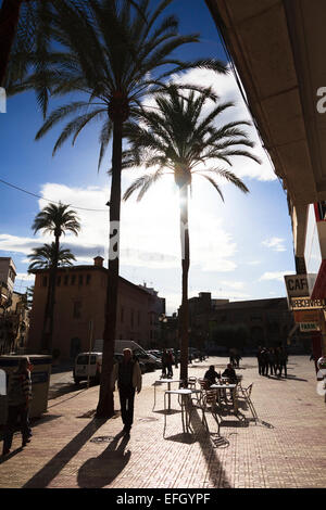 Sun silhouetting palm trees and cafe tables in a Spanish Plaza Stock Photo