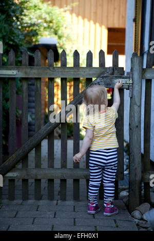 Toddler opening a wooden garden gate. Stock Photo