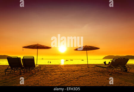 Retro filtered picture of beach chairs and umbrellas on sand at sunset. Concept for rest, relaxation, holidays. Stock Photo