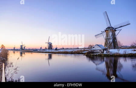 Sunrise over the windmills at the famous dutch UNESCO site Kinderdijk on a cold morning with reflection in the water. Stock Photo