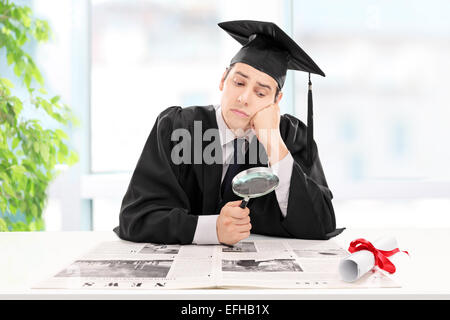 Student looking for a job in a newspaper at home with a magnifying glass Stock Photo