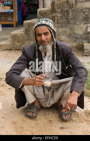 Old man squatting whilst drinking tea and smoking a cigarette, at Chisapani Village, on the Royal Trek, near Pokhara, Nepal Stock Photo
