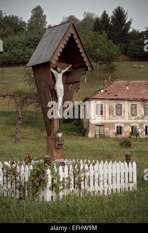 Jesus at cross in front of deserted house, rural Krsko, Dolenjska, Bela Krajina, Slovenia Stock Photo