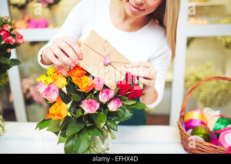 Young florist putting love note in small envelope in fresh rose bouquet Stock Photo