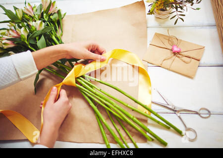 Hands of Caucasian woman wrapping bouquet in brown paper stock photo