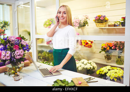 Friendly shop assistant speaking on the phone and using laptop in the shop Stock Photo